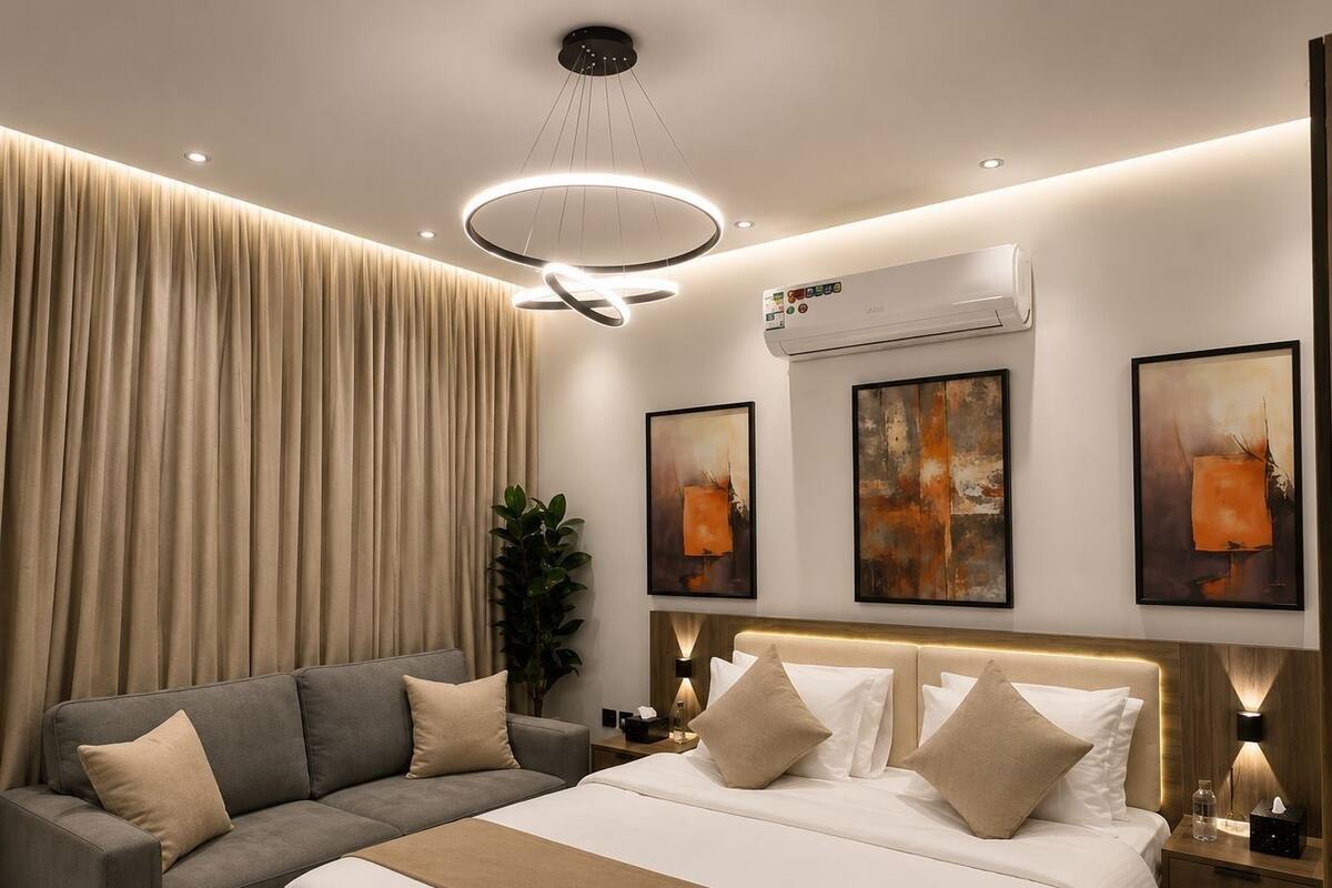A modern hotel room with a bed, a sofa, an air conditioning unit, and artwork on the walls.