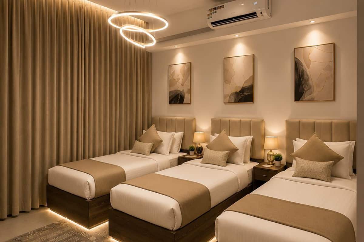 A hotel room with three beds, a large window with curtains, a modern chandelier, and an air conditioning unit.
