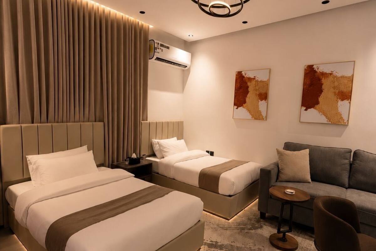 A modern hotel room with two beds, a sofa, a small table, and abstract wall art.