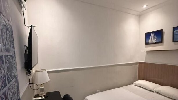 Une chambre d’hôtel comprenant un lit, un bureau avec une chaise, une lampe et un téléviseur fixé au mur.