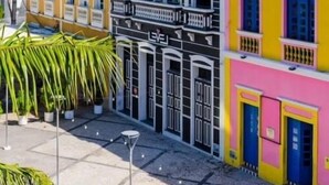 Une rangée de bâtiments colorés dotés de balcons, un ciel dégagé et une zone pavée agrémentée de plantes en pot.