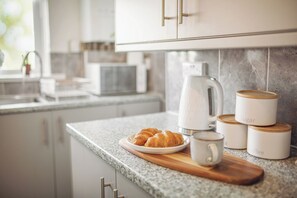 Eine Küchenarbeitsplatte mit Croissants, einer Kaffeetasse sowie Zucker- und Kaffeedosen.