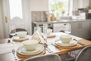 A dining table set with plates, bowls, cutlery, and glasses, with a kitchen in the background. - Central Luxe Stylish House | Free Parking | 10PPL (Sheffield)