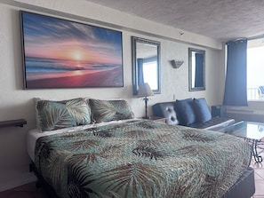 A bedroom with a large bed, a desk, a chair, and a large painting of a sunset. - Coffee on the Balcony * Sunrise's * Relaxation (Daytona Beach)