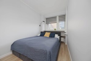 Ein Schlafzimmer mit einem Bett, einem Fenster mit Jalousien, einem Nachttisch und einer Heizung.