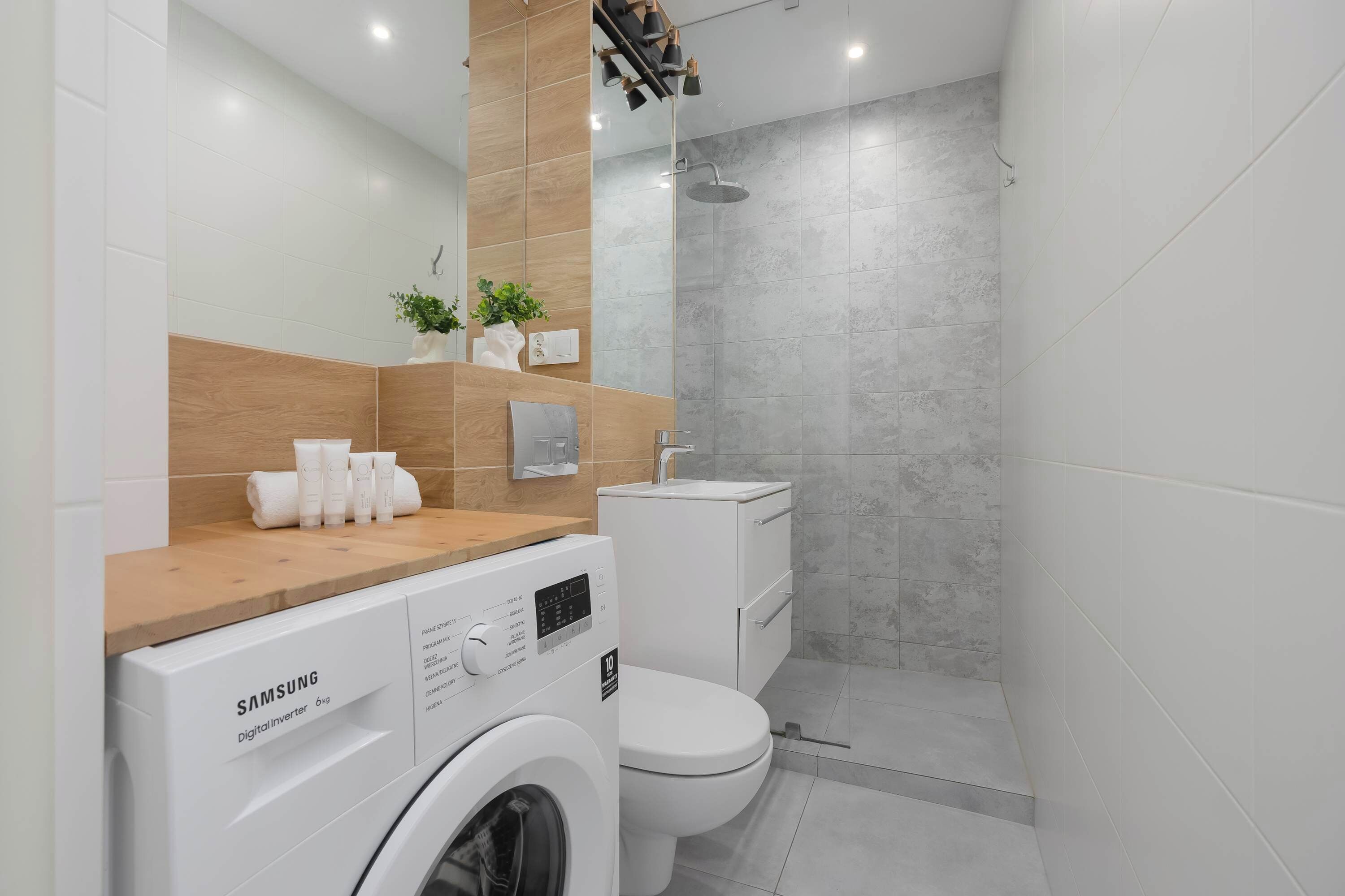 A modern bathroom with a Samsung washing machine, a toilet, and a shower area.