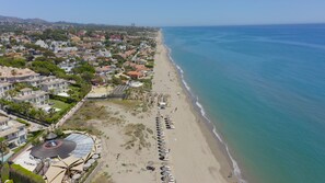 An aerial view of a coastal area with a beach, hotel buildings, and a clear blue sea.