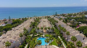 A resort with a central pool surrounded by palm trees and Mediterranean-style buildings.
