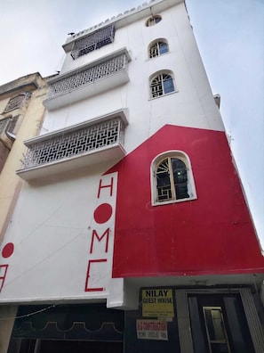 A multi-story building with balconies, a red and white facade, and a sign indicating a guest house.