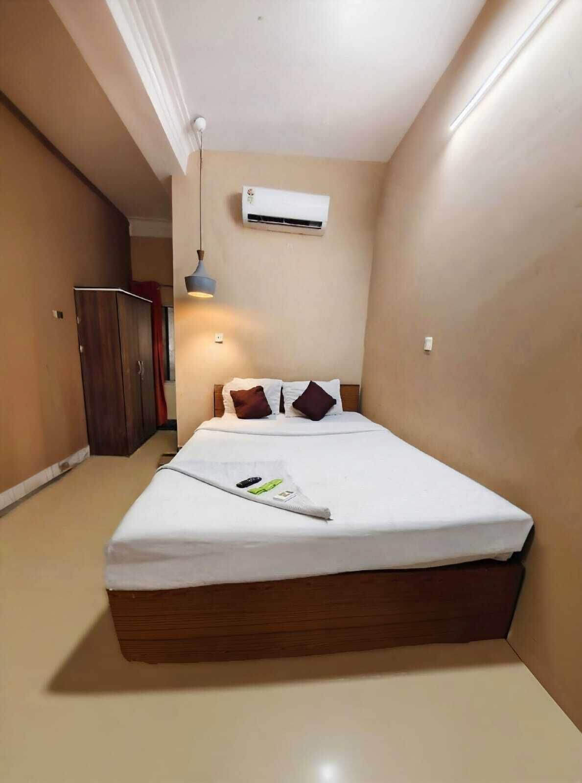 A small, neatly arranged bedroom with a single bed, a wardrobe, and an air conditioning unit on the wall.