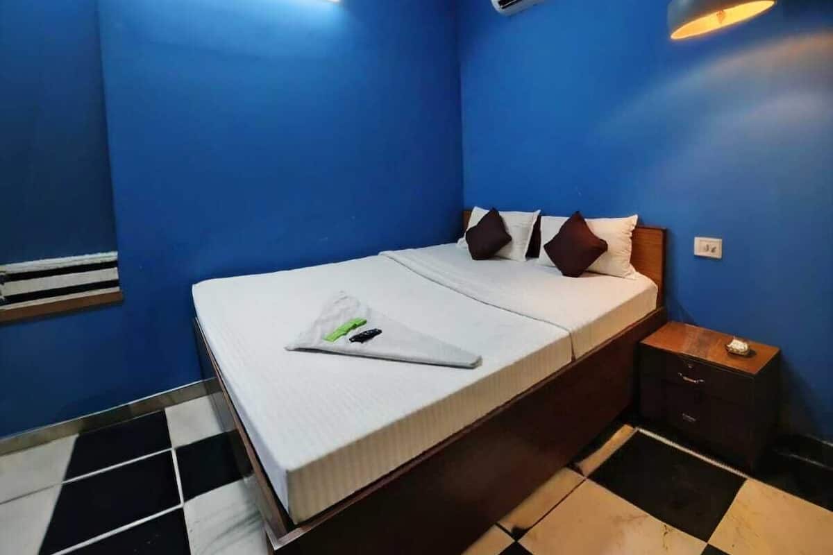 Une chambre comprenant un lit, une table de chevet, un climatiseur fixé au mur et un luminaire au plafond.