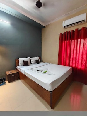 A hotel room with a bed, bedside table, and an air conditioning unit. - Nilay Guest House (Kolkata)