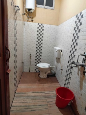 A small bathroom with a toilet, a red bucket, and tiled walls.