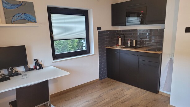 Eine moderne Küche mit Holz Arbeitsplatte, schwarzen Schränken, einem Fenster mit Jalousien und einem Dell-Monitor auf einem Schreibtisch.