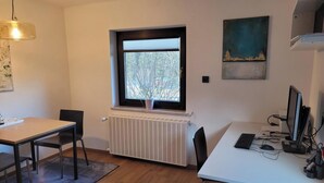Ein Zimmer mit einem weißen Heizkörper, einem Fenster mit Jalousien, einem Schreibtisch mit einem Computer und einem Stuhl.
