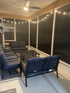 Ein Wintergarten mit Deckenventilator, Lichterketten, einer Couch, einem Couchtisch und großen Fenstern.