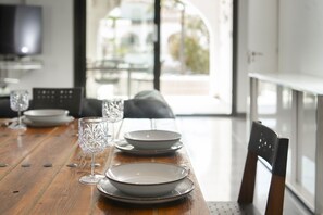 Ein Esstisch mit Tellern, Gläsern und einem Stuhl in einem modernen Interieur mit Blick durch eine Glastür.