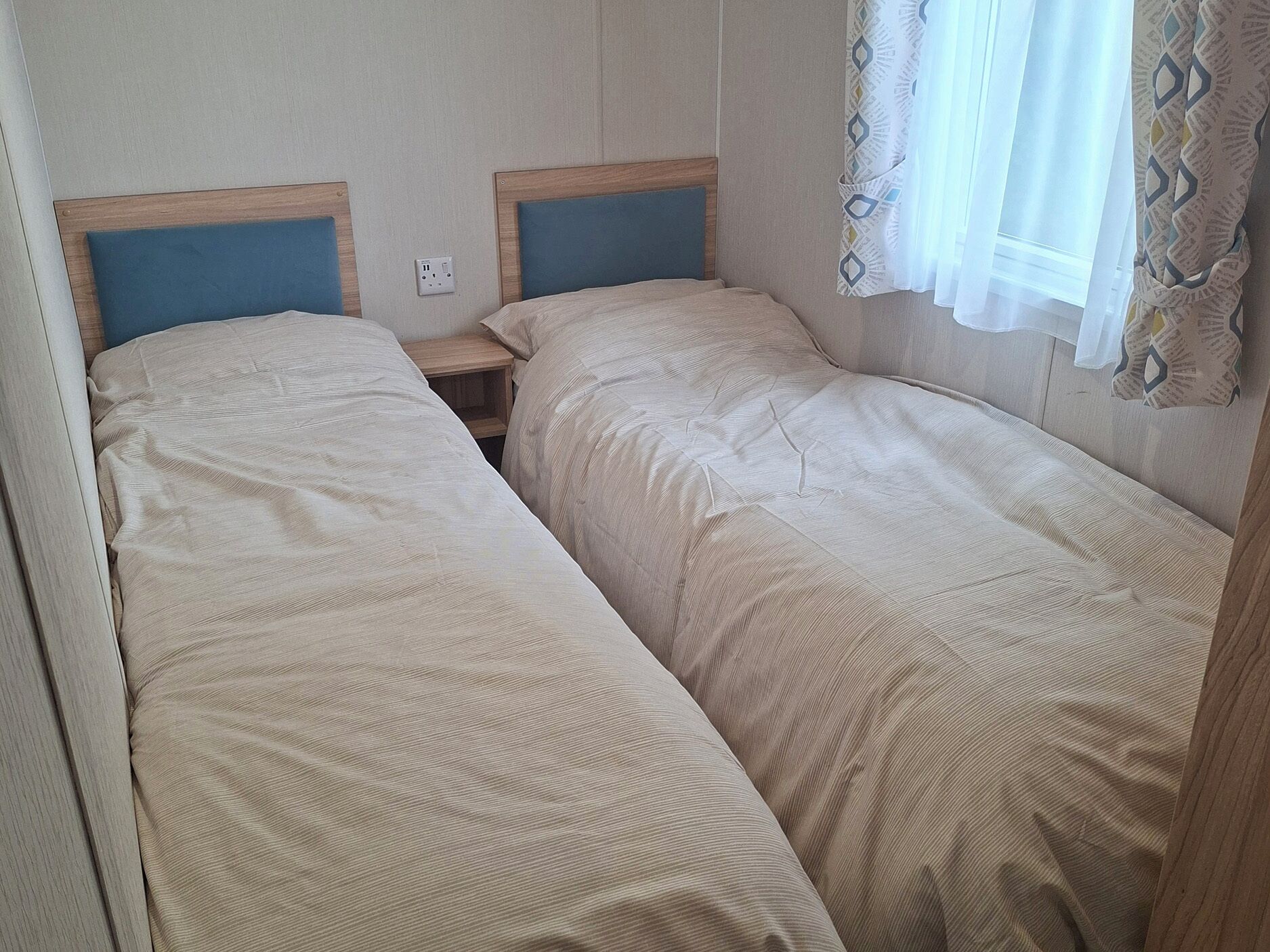 A twin room with two beds, a nightstand, and a window with curtains.