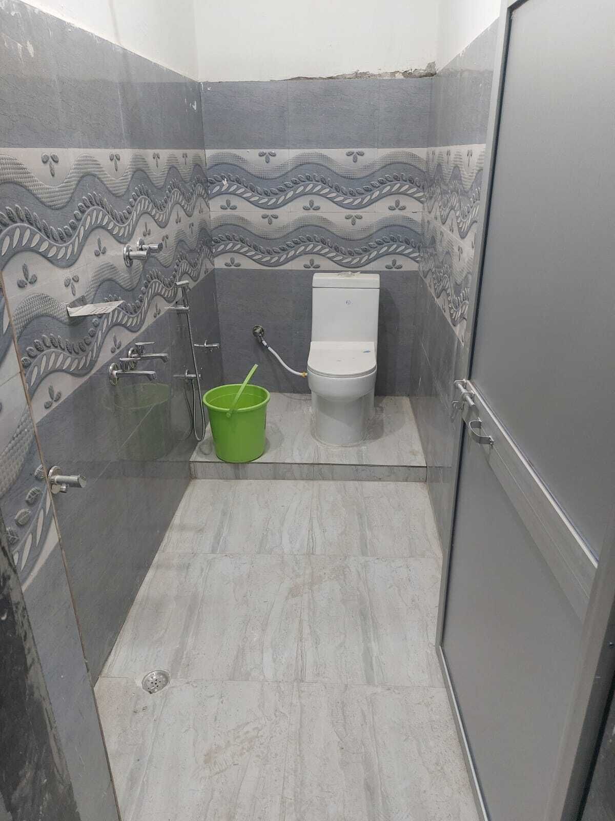 A small bathroom with a toilet, shower, and a green bucket.