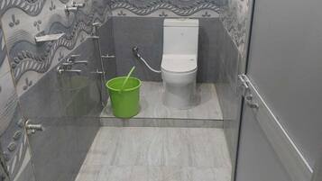 A small bathroom with a toilet, shower, and a green bucket.