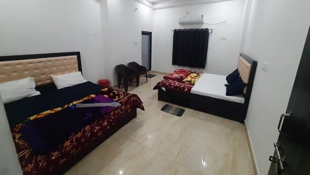 A room with two beds, a ceiling fan, an air conditioning unit, and a door. - Hotel Anuj Palace ll Near Ram Mandir - Comfortable AC Stay (Ayodhya)