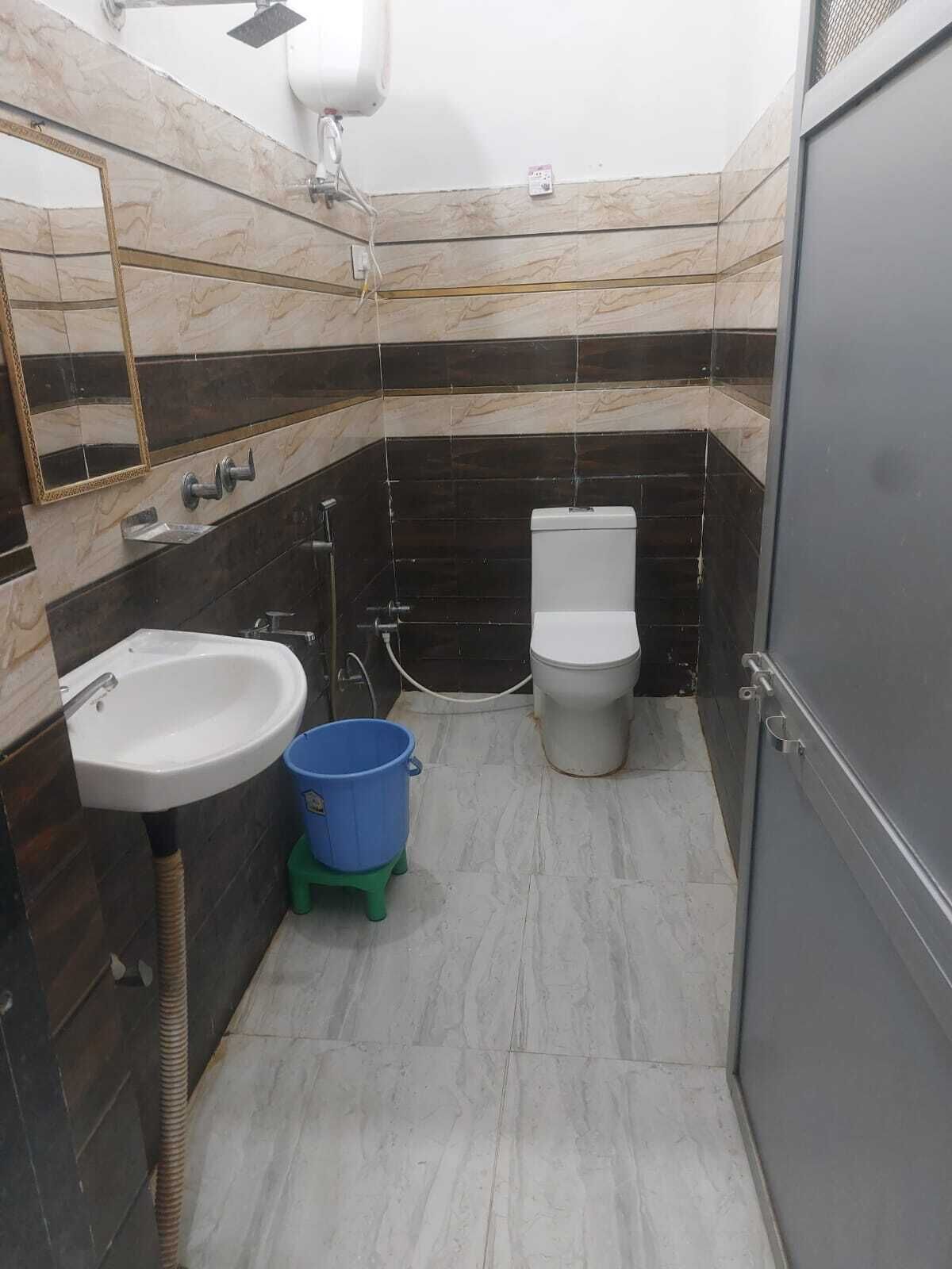 A bathroom with a sink, toilet, and blue bucket on a stool.