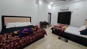 A hotel room with two beds, a ceiling fan, and a window with curtains. - Hotel Anuj Palace ll Near Ram Mandir - Comfortable AC Stay (Ayodhya)
