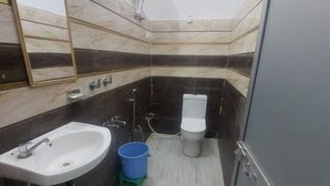 A small bathroom with a sink, mirror, toilet, and a blue bucket on the floor. - Hotel Anuj Palace ll Near Ram Mandir - Comfortable AC Stay (Ayodhya)