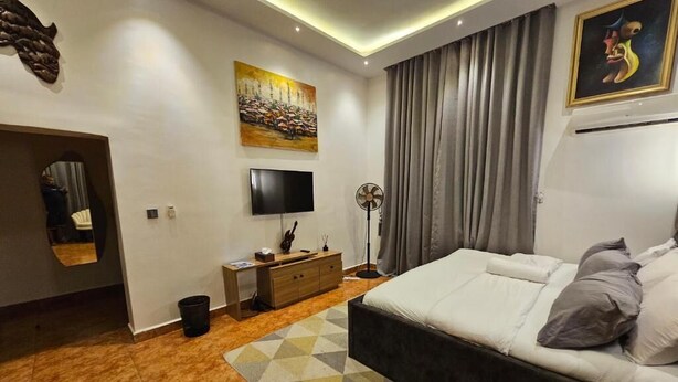 Ein modernes Schlafzimmer mit einem großen Bett, einem Flachbildfernseher, einem Standventilator und einem Bild an der Wand.
