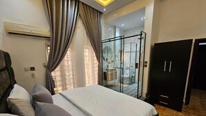 Ein modernes Hotelzimmer mit einem großen Bett, einer Duschkabine aus Glas und einem Kleiderschrank.