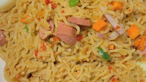 Ein Teller Nudeln mit Gemüse und Fleisch, dazu ein gekochtes Ei und Gurkenscheiben.