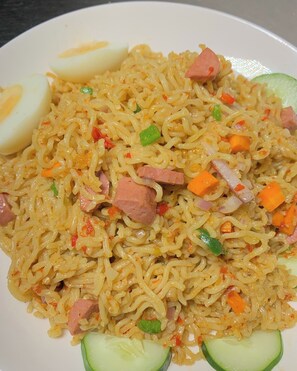 A plate of noodles with vegetables and meat, accompanied by a boiled egg and cucumber slices.