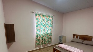 Un dormitorio con cama, mesita de noche, armario de pared y ventana con cortina floral.