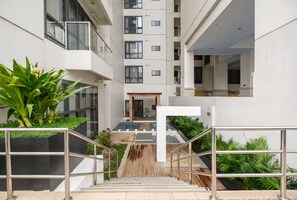 Ein modernes Gebäude mit einer zentralen Treppe, die zu einem Poolbereich führt, umgeben von Grünflächen und Balkonen.
