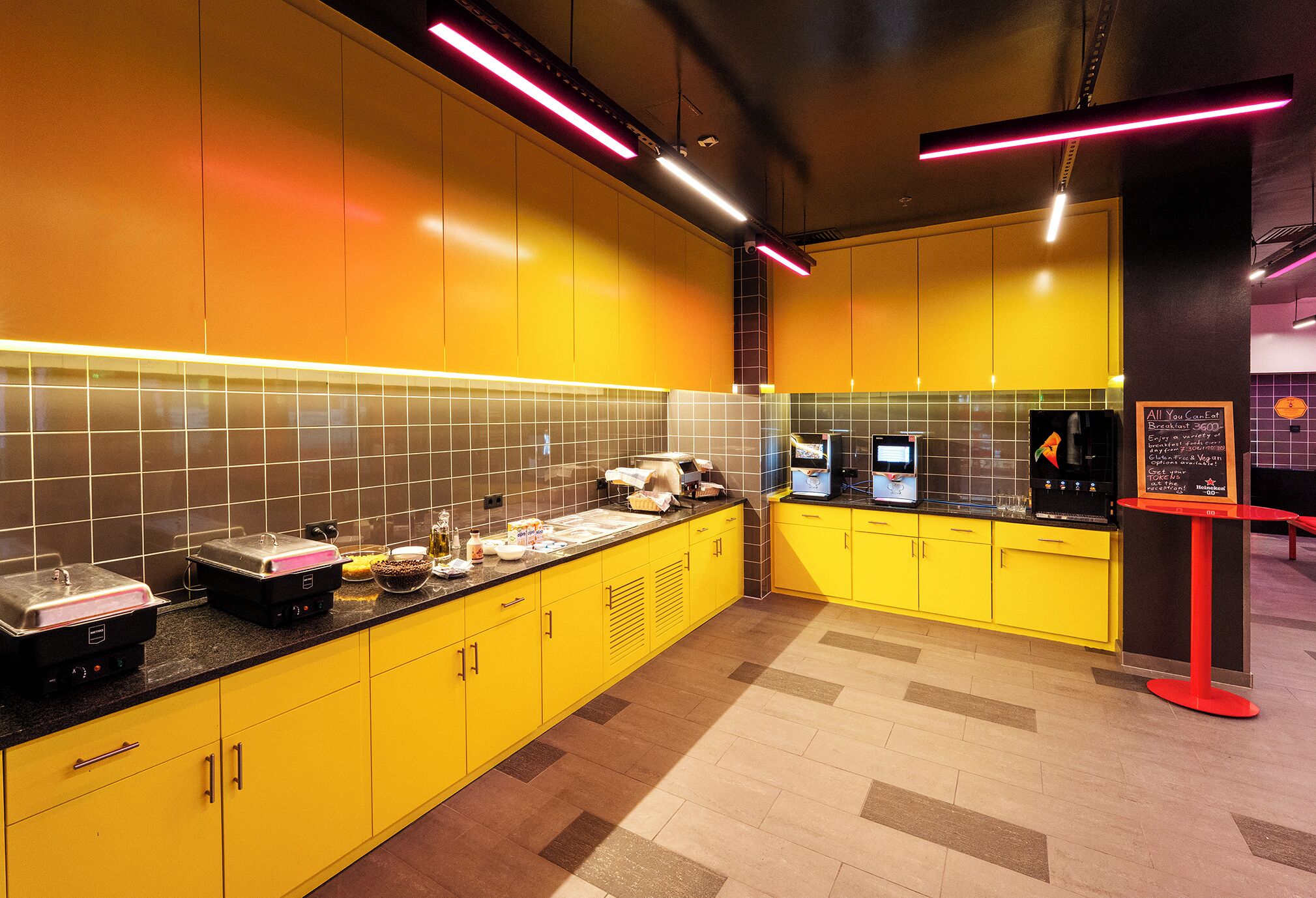 A modern kitchen with yellow cabinets, a black countertop, and a menu board.