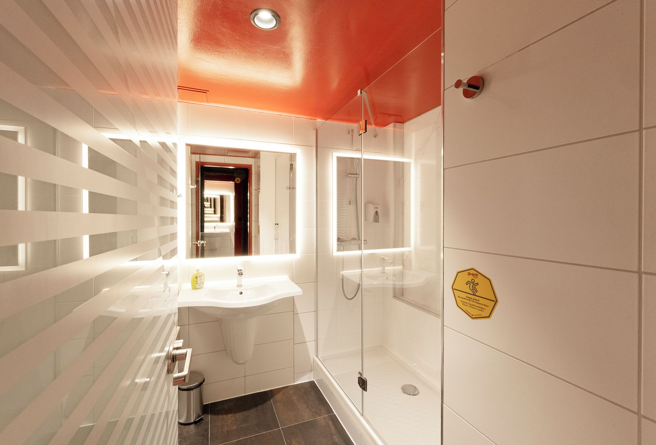 A modern bathroom with a glass shower enclosure, a sink with a mirror, and a tiled floor.
