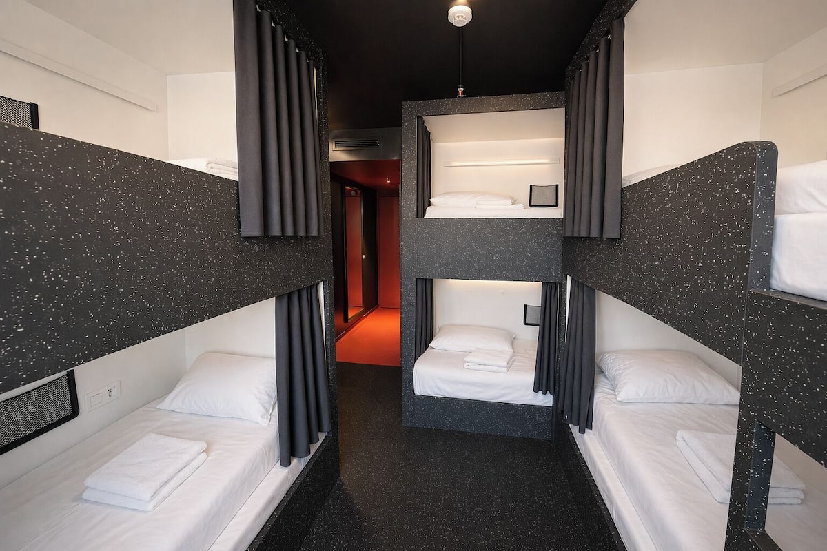 A bunk room with three bunk beds, a small bedside table, and a wall-mounted light fixture.