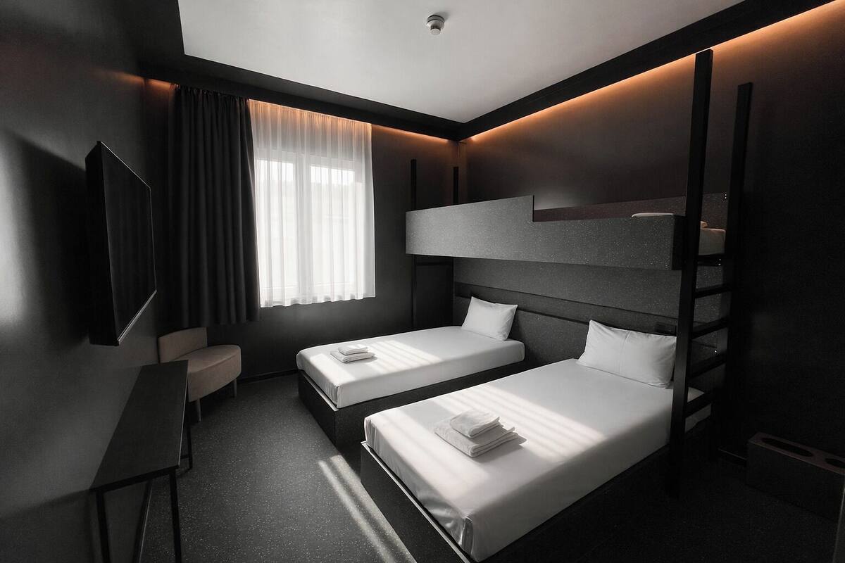 A modern hotel room with two single beds, a desk, a chair, a TV, and a window with curtains.