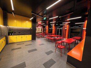 Un restaurante moderno con decoración amarilla y roja, varias mesas y una señal de salida visible.