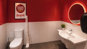 Une salle de bain moderne aux couleurs rouge et blanche, comprenant des toilettes, un bidet, un lavabo et un miroir avec un éclairage circulaire.