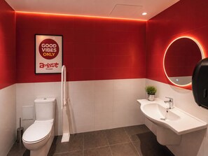 Een moderne badkamer in het rood en wit, met een toilet, een bidet, een wastafel en een spiegel met ronde verlichting.