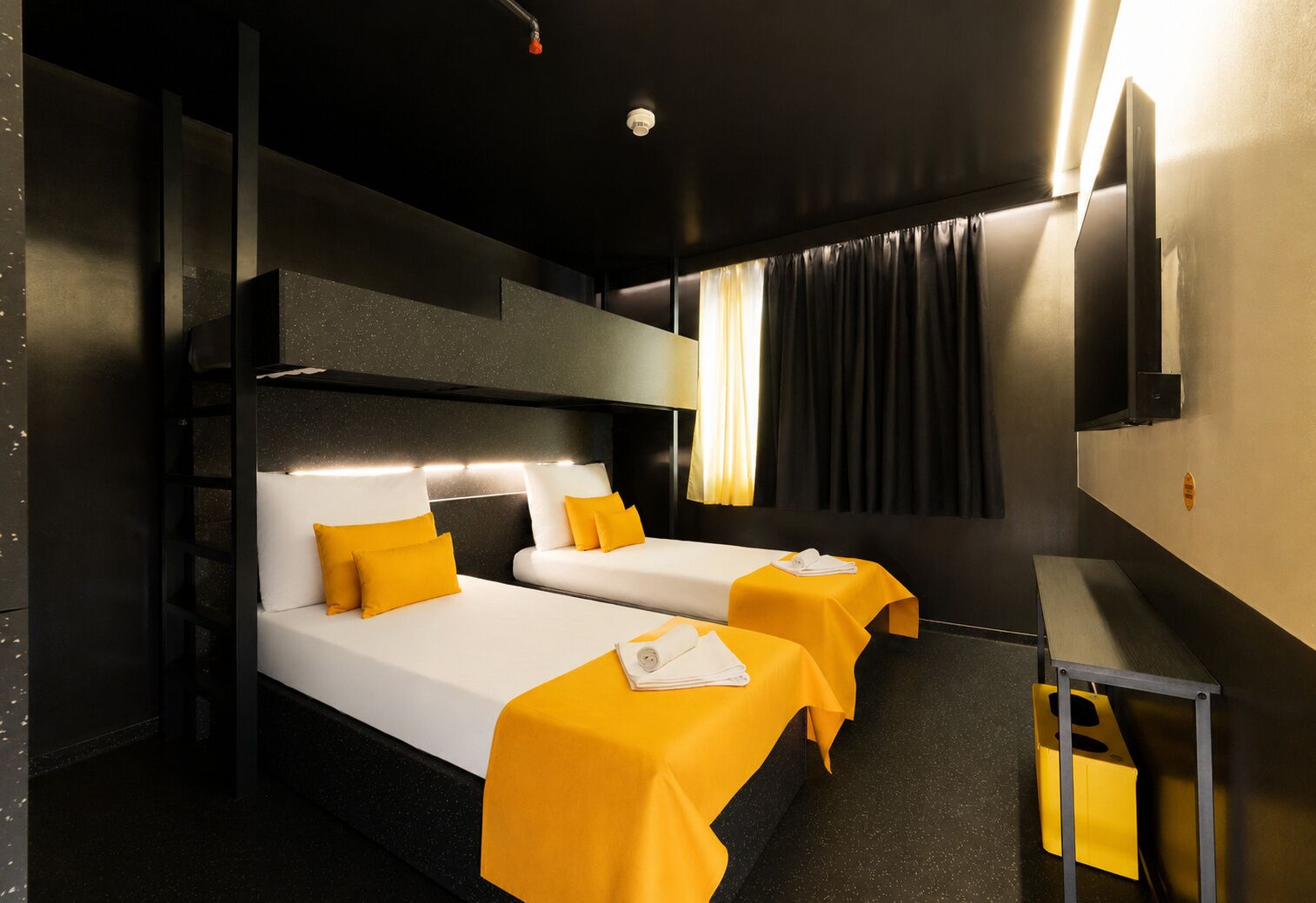 A hotel room with two beds, a small table, a bench, and a mirror.