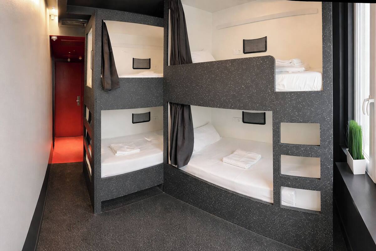 A bunk bed room with a red door, a small plant, and a window with curtains.