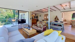Un soggiorno moderno con un televisore grande, un divano, un'area pranzo e una cucina visibile attraverso una porta aperta.