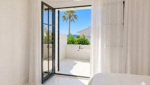 Una habitación con puerta de vidrio corrediza que da a un balcón exterior con una palmera y una valla blanca.