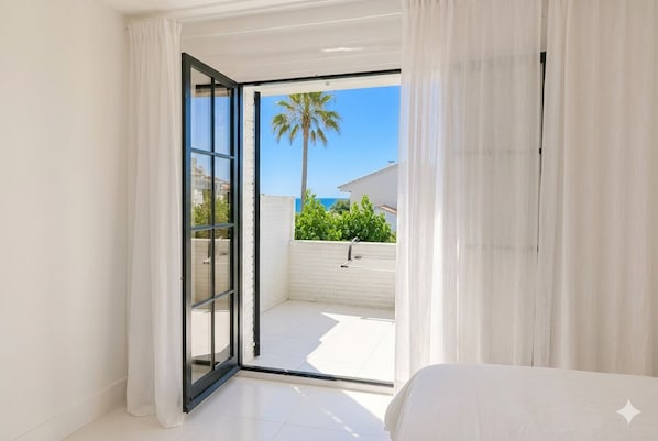 Una habitación con puerta de vidrio corrediza que da a un balcón exterior con una palmera y una valla blanca.