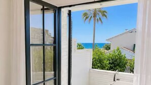 Habitación con puerta de cristal corredera que da a un balcón con suelo de baldosas blancas y vistas al océano.