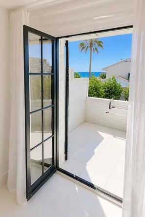 A room with a sliding glass door leading to a balcony with a white tiled floor and a view of the ocean.