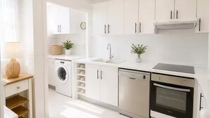 Una cocina moderna con armarios blancos, lavadora, lavavajillas y horno.