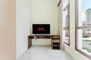 Ein Zimmer mit Fernseher auf einem Holztisch, einem Fenster mit Blick auf Gebäude und einem Fliesenboden.